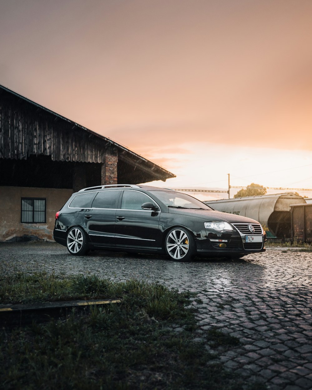 black sedan parked beside brown wooden house during sunset