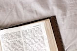 An open book lays on a white fabric surface. The book is open to the page with the title 'MALACHI 3:1' at the top. The text is in black font with some of the words highlighted in red, possibly signifying importance or emphasis. The book has a brown cover that can be partially seen in the image.