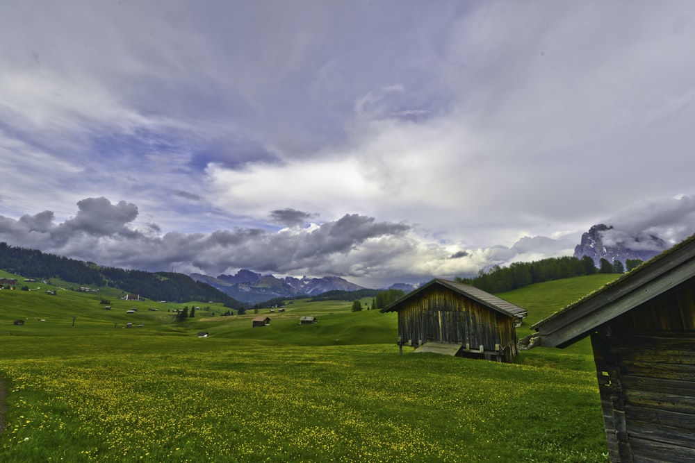 casa de madera marrón en campo de hierba verde bajo nubes blancas y cielo azul durante el día