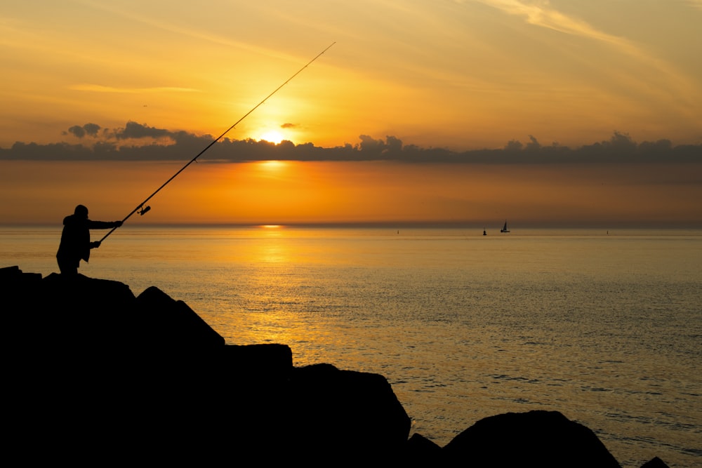 Silueta de la persona que pesca en el mar durante la puesta del sol