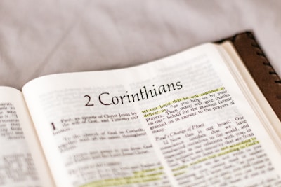 An open book displaying a page from the Bible, specifically from the book of 2 Corinthians. The text includes paragraphs and highlighted passages with yellow marker. The focus is primarily on the printed and highlighted text.