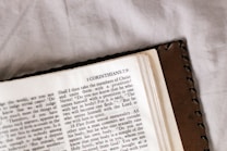An open book featuring a page from the Bible with text from 1 Corinthians 7:9. The book has a brown leather cover and is resting on a light-colored surface.