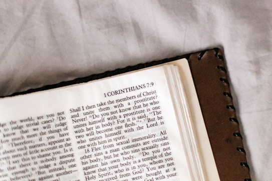 An open book featuring a page from the Bible with text from 1 Corinthians 7:9. The book has a brown leather cover and is resting on a light-colored surface.
