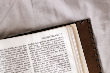 An open book featuring a page from the Bible with text from 1 Corinthians 7:9. The book has a brown leather cover and is resting on a light-colored surface.
