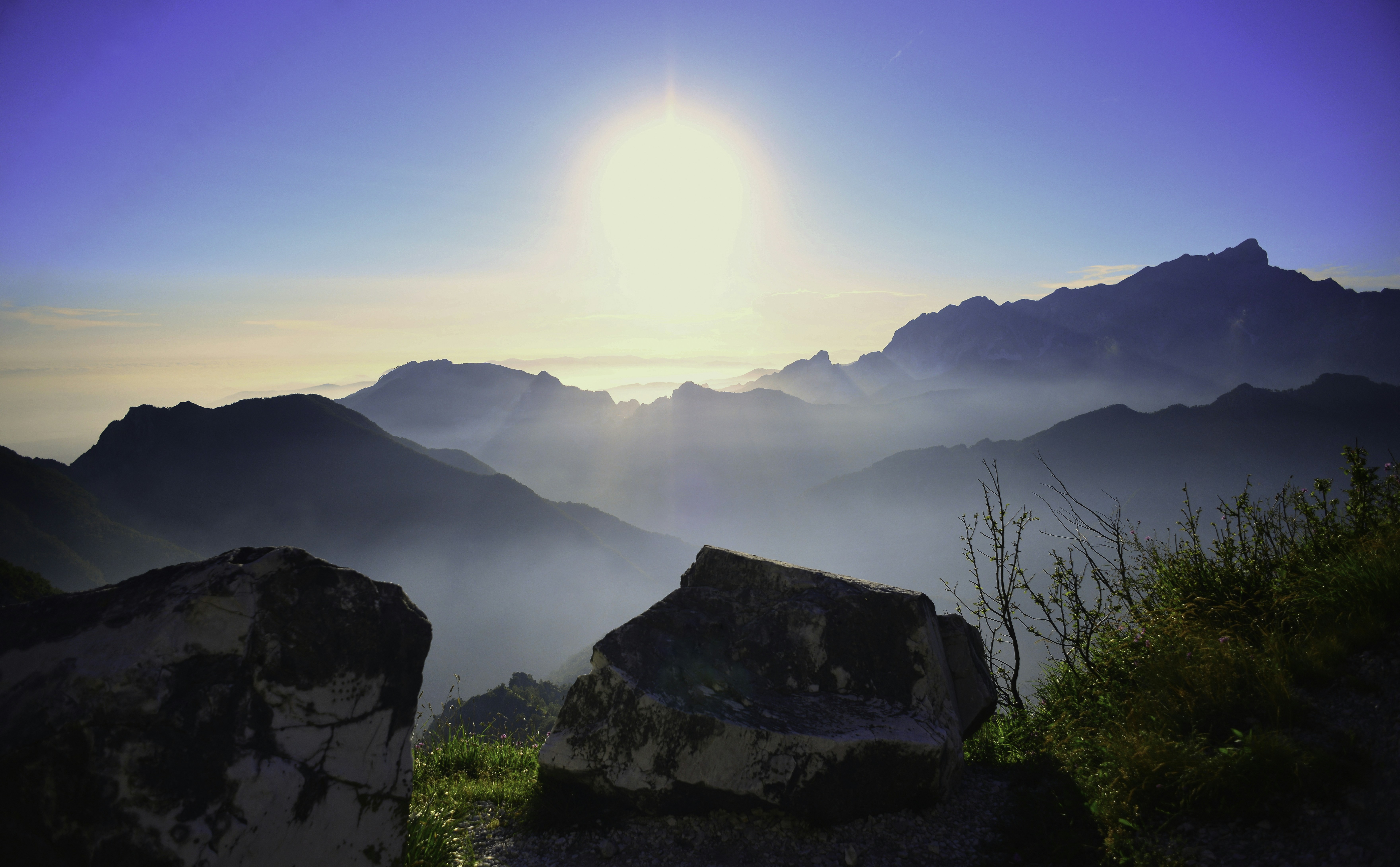 Il sole filtra attraverso la nebbia di montagna all'alba su cime frastagliate.