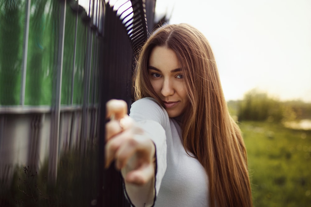 Femme en chemise à manches longues blanche debout près d’une clôture en métal vert pendant la journée