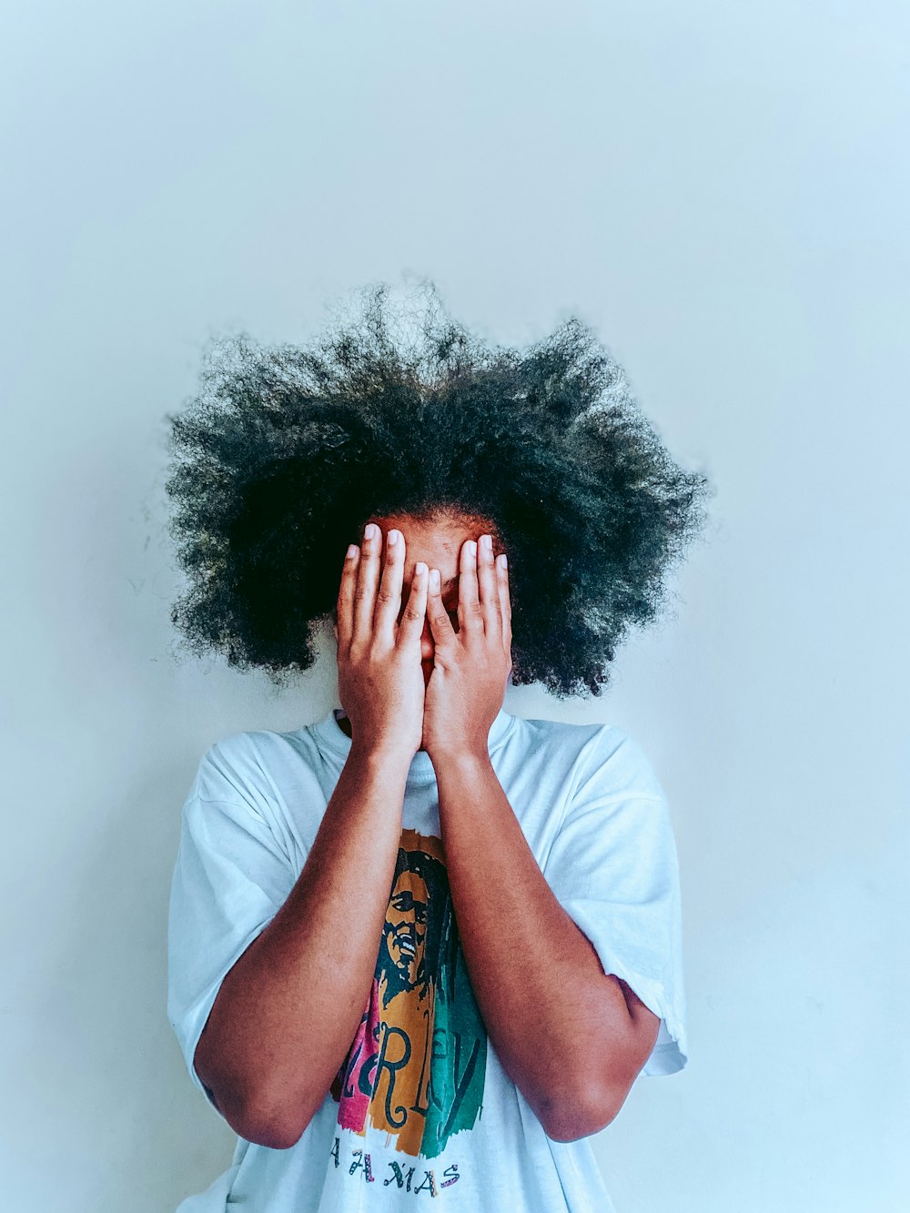 man in white t-shirt covering his face with his hair