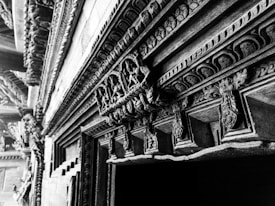 Ornate and intricate wooden carvings adorn a structure, displaying detailed patterns and craftsmanship. The carvings include floral and geometric motifs along a wooden beam or doorway, highlighting the skill and artistry involved.