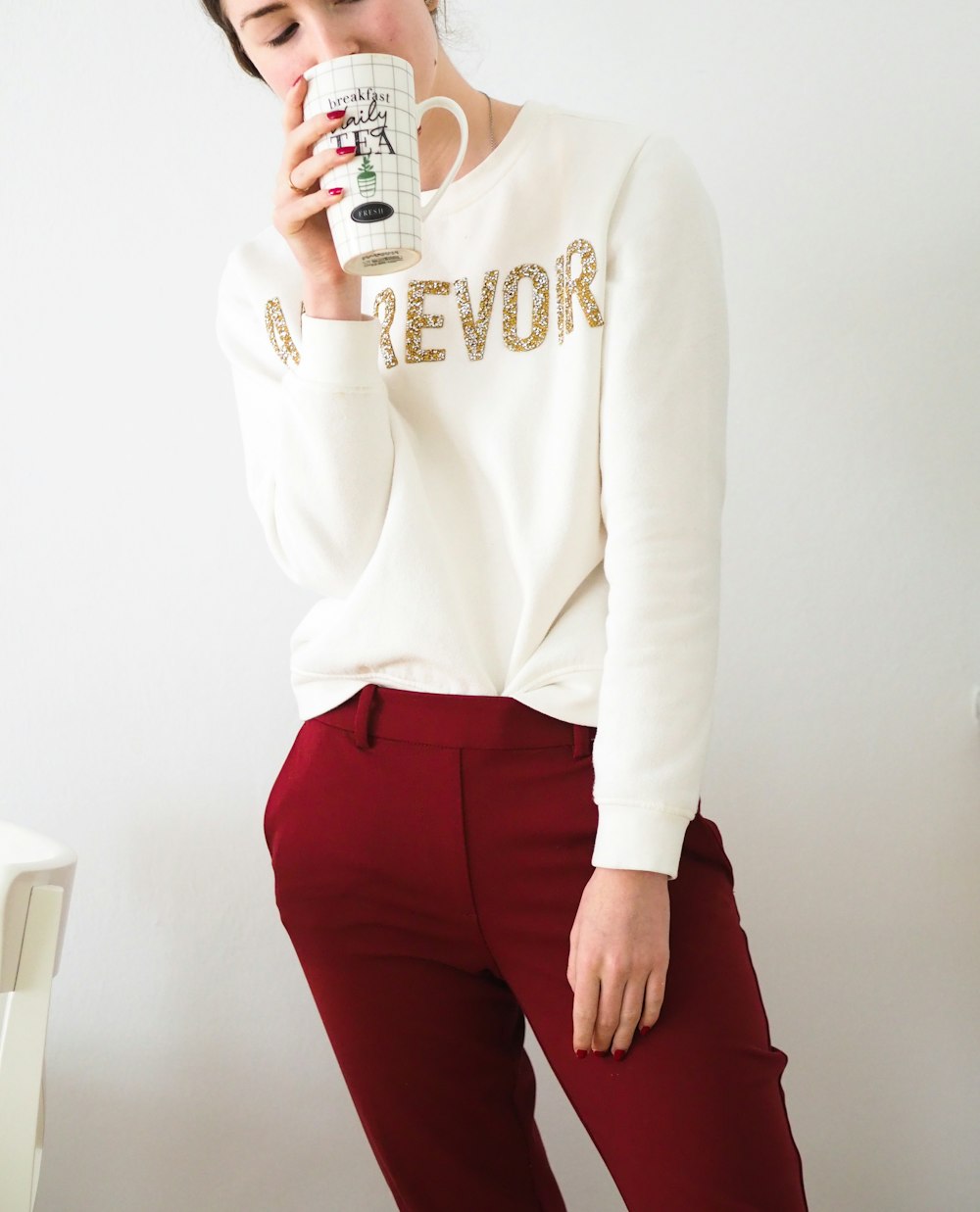 woman in white long sleeve shirt and red pants holding white ceramic mug