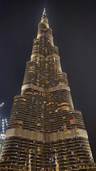 A towering commercial skyscraper reflecting the city skyline at dusk, with glowing windows and strong steel framework.