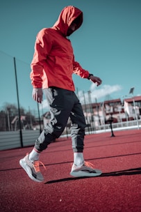 man in red hoodie and black pants running on track field during daytime