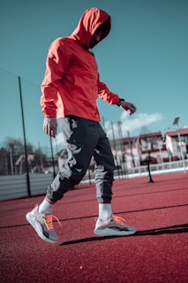 man in red hoodie and black pants running on track field during daytime