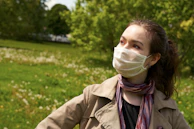 A smiling person wearing a pastel-colored aerisana mask while walking through a sunny park.