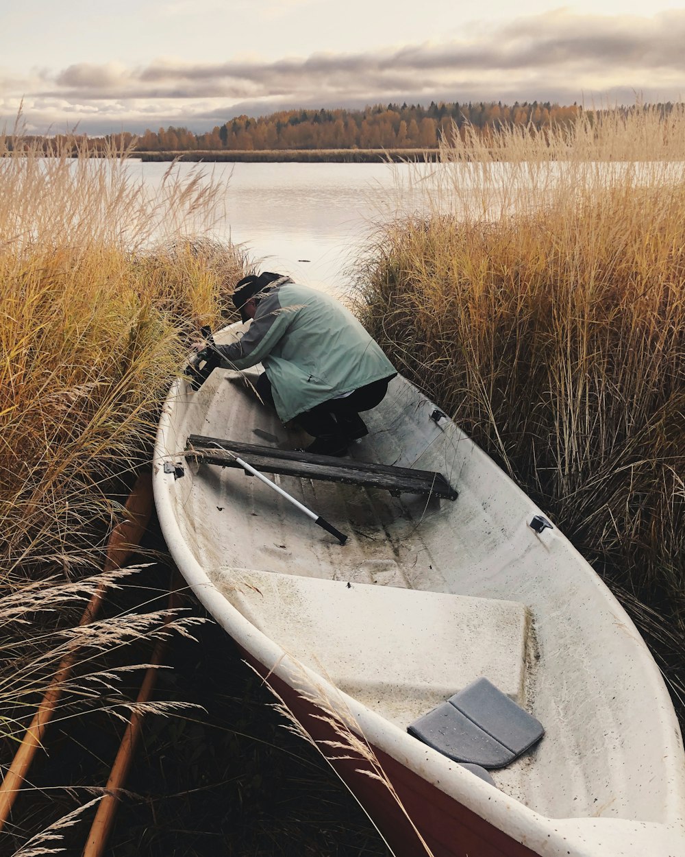 man in gray jacket riding white canoe on brown grass field during daytime