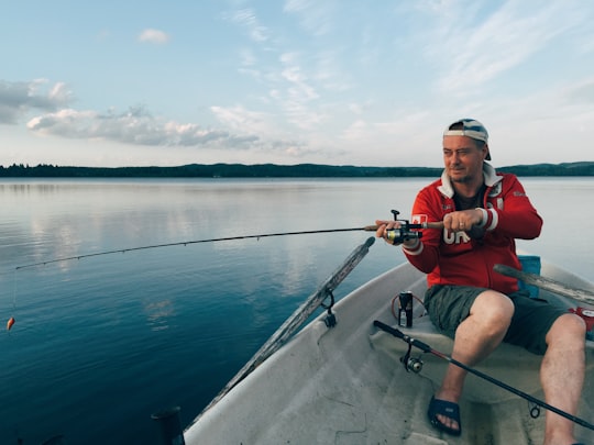man in red shirt and black shorts sitting on boat holding fishing rod during daytime in Orivesi Finland