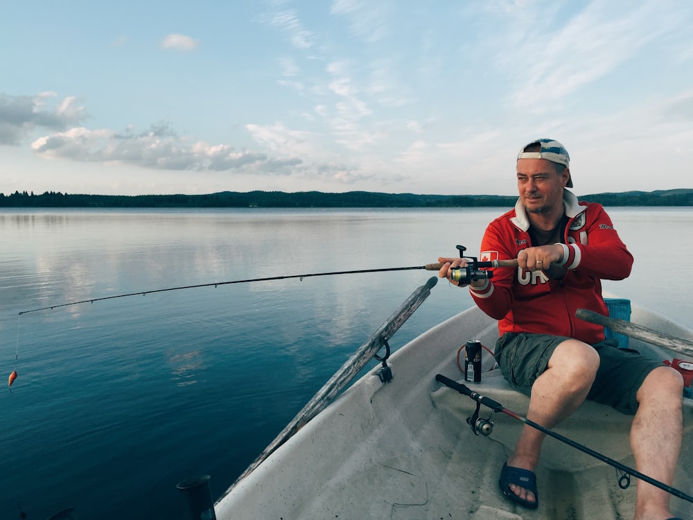 homme en chemise rouge et short noir assis sur un bateau tenant une canne à pêche pendant la journée