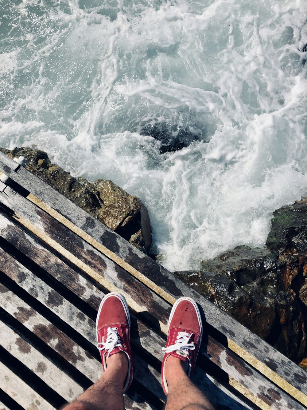 Persona in scarpe da ginnastica rosse e bianche in piedi sul molo di legno sopra l'acqua