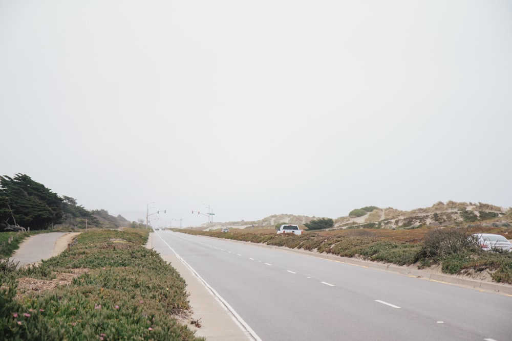 gray concrete road between green grass field during daytime