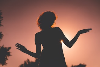 silhouette of woman raising her hands during sunset
