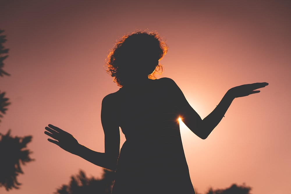 silhouette of woman raising her hands during sunset