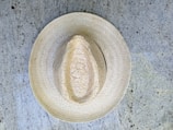 A straw hat placed on a textured, speckled concrete surface. The hat exhibits intricate woven patterns, showcasing craftsmanship and traditional design.