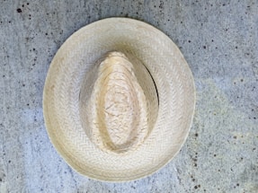 A straw hat placed on a textured, speckled concrete surface. The hat exhibits intricate woven patterns, showcasing craftsmanship and traditional design.