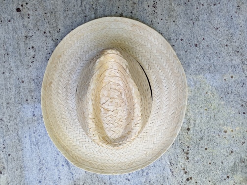 A straw hat placed on a textured, speckled concrete surface. The hat exhibits intricate woven patterns, showcasing craftsmanship and traditional design.