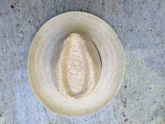 A straw hat placed on a textured, speckled concrete surface. The hat exhibits intricate woven patterns, showcasing craftsmanship and traditional design.