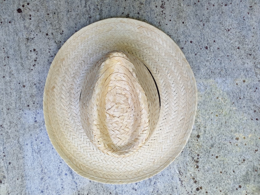 A straw hat placed on a textured, speckled concrete surface. The hat exhibits intricate woven patterns, showcasing craftsmanship and traditional design.