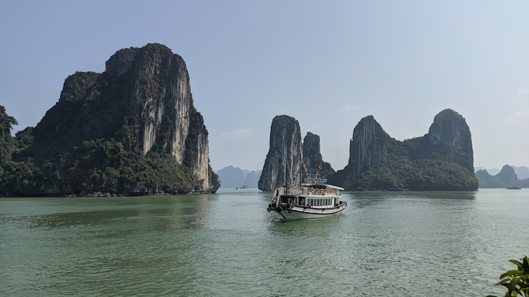A vibrant boat tour gliding through mangrove forests with limestone karsts towering in the background under a bright blue sky.