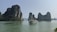 A scenic view of towering limestone islands covered with lush greenery rises from calm, turquoise waters. A traditional boat with a flag and several passengers sails across the water, creating a serene landscape.