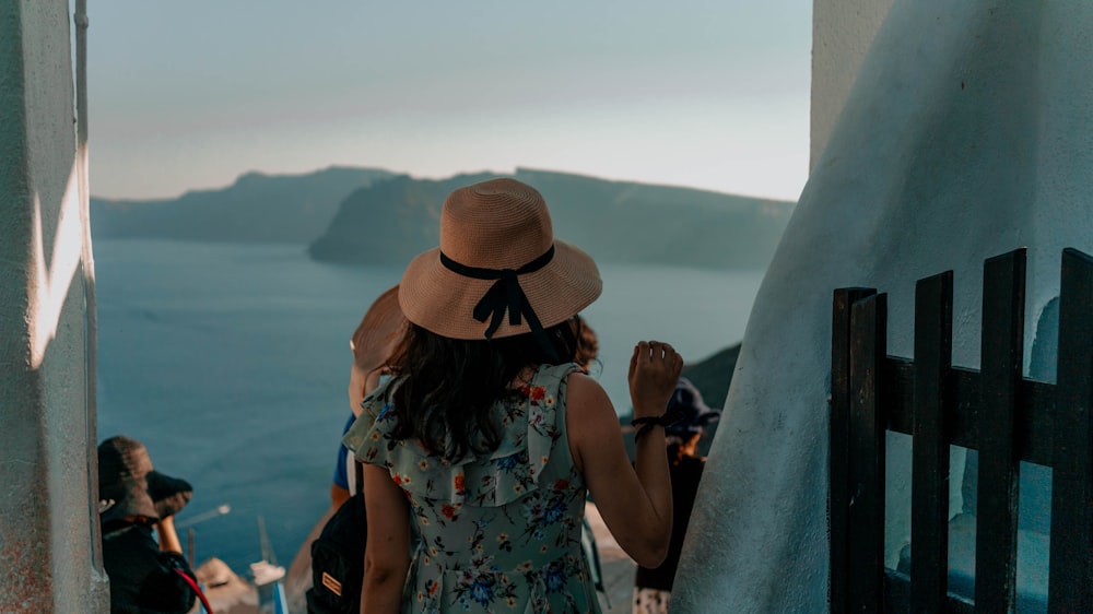 woman in blue and white floral sleeveless dress wearing brown fedora hat standing on beach during