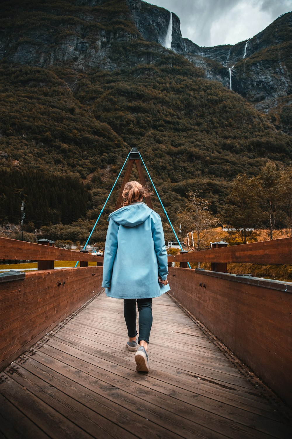 woman in teal coat walking on wooden bridge during daytime
