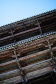 Wooden architectural structure with multiple horizontal beams and intricately detailed design, set against a clear blue sky.