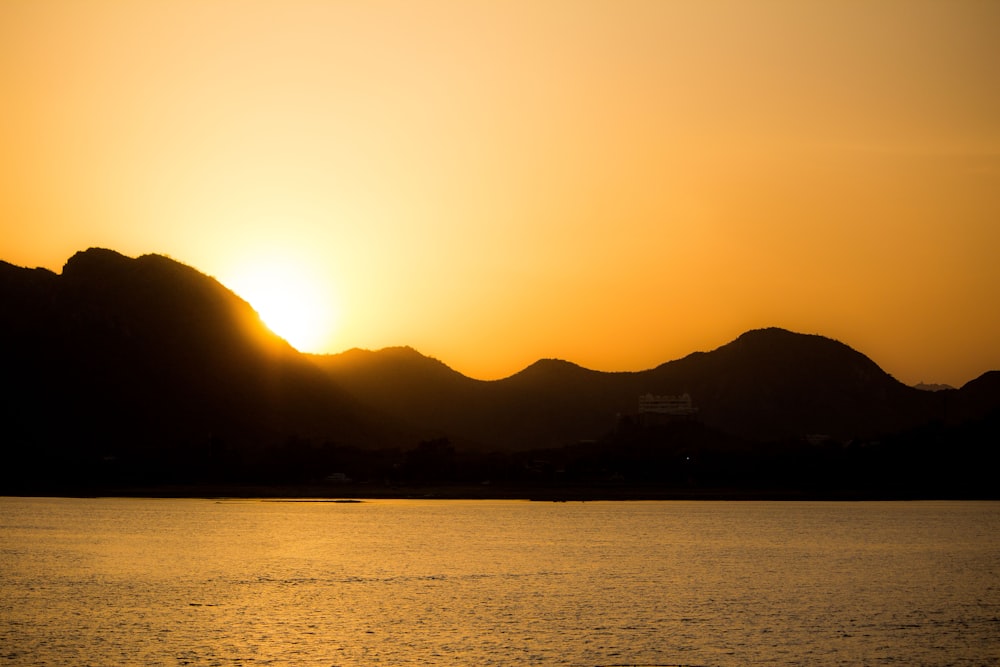 silhouette of mountain near body of water during sunset