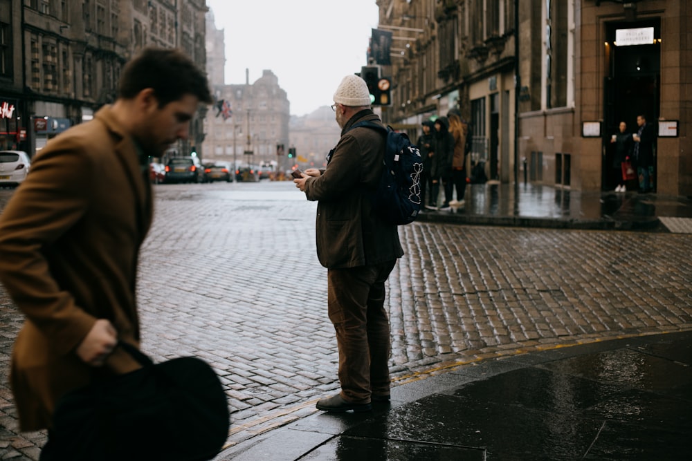 man in black jacket and brown pants walking on sidewalk during daytime