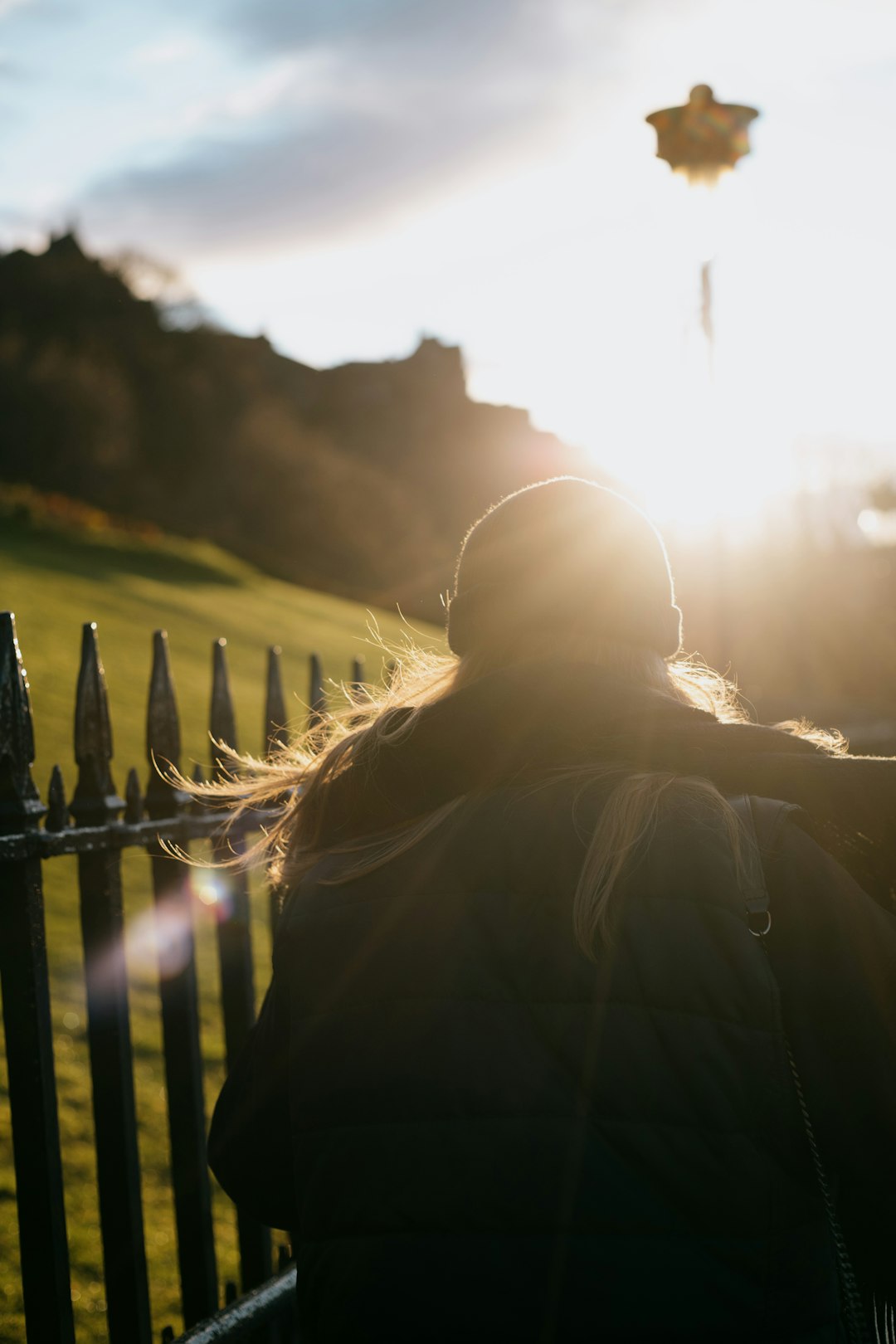 woman in black jacket standing near fence during sunset