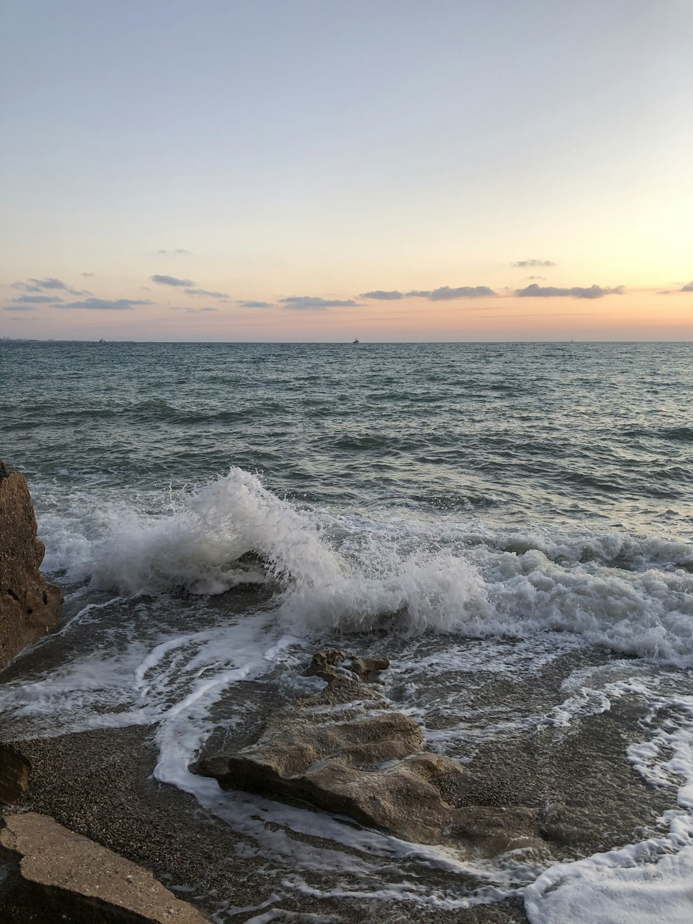 ocean waves crashing on brown rocky shore during sunset