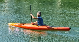 man in blue shirt riding orange kayak on lake during daytime