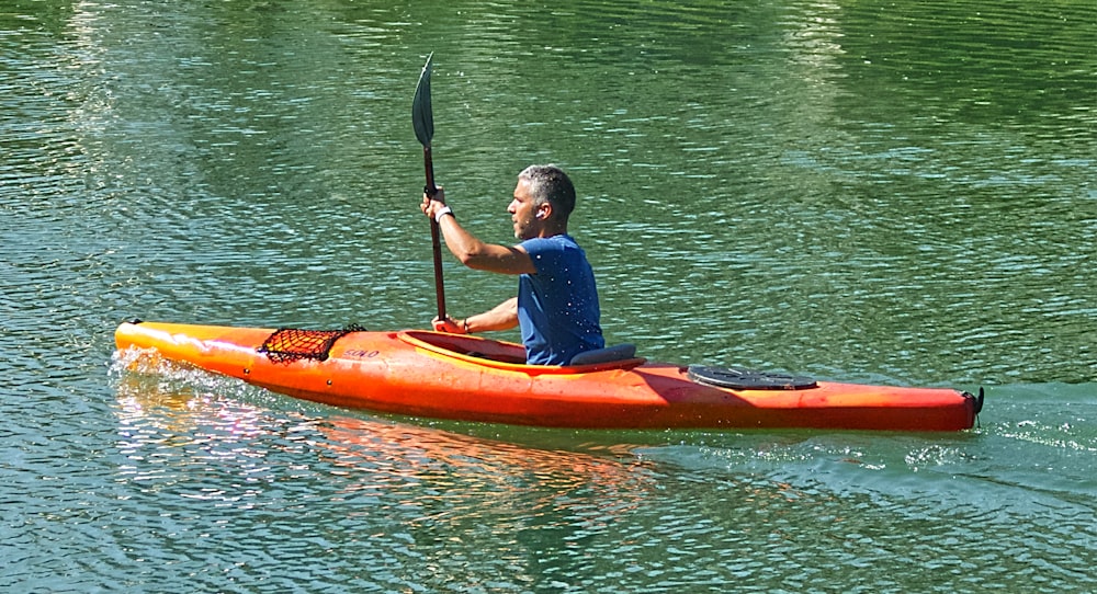 Uomo in camicia blu che cavalca il kayak arancione sul lago durante il giorno
