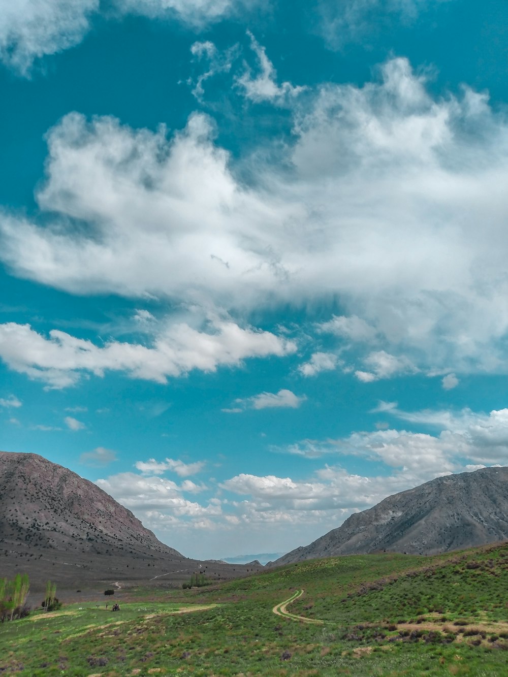 green grass field and mountains under blue sky and white clouds during daytime