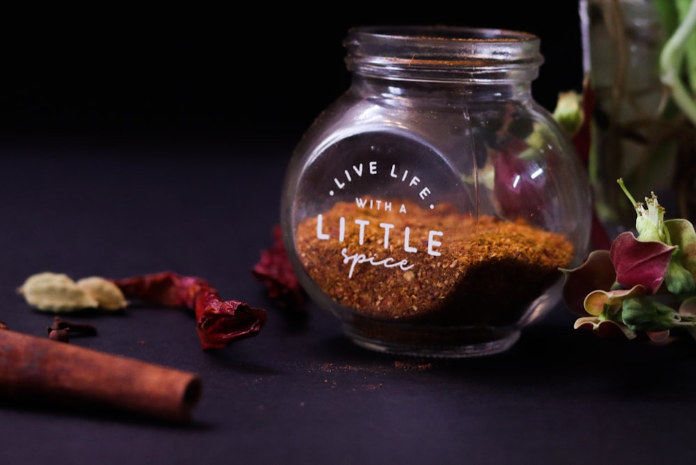 a glass jar filled with spices next to a flower