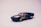 A toy car modeled after a classic muscle car with a dark blue body featuring yellow flame decals on the sides. The car has chrome-like details on the hood, resembling an engine, along with shiny wheels that have a star-like design. The background is a soft gradient from pink to white, providing a clean and focused backdrop.
