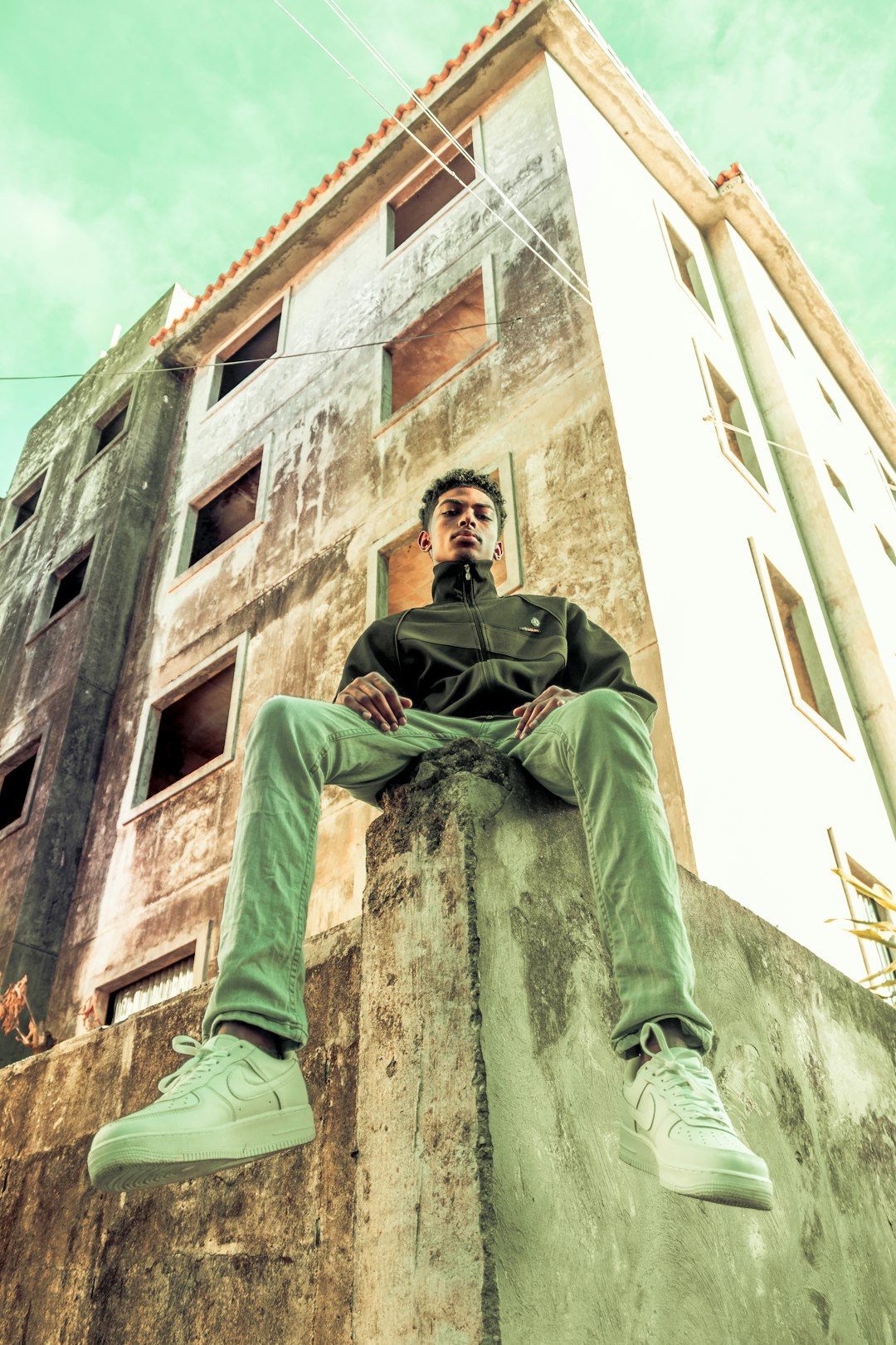 man in green jacket and pants sitting on concrete wall