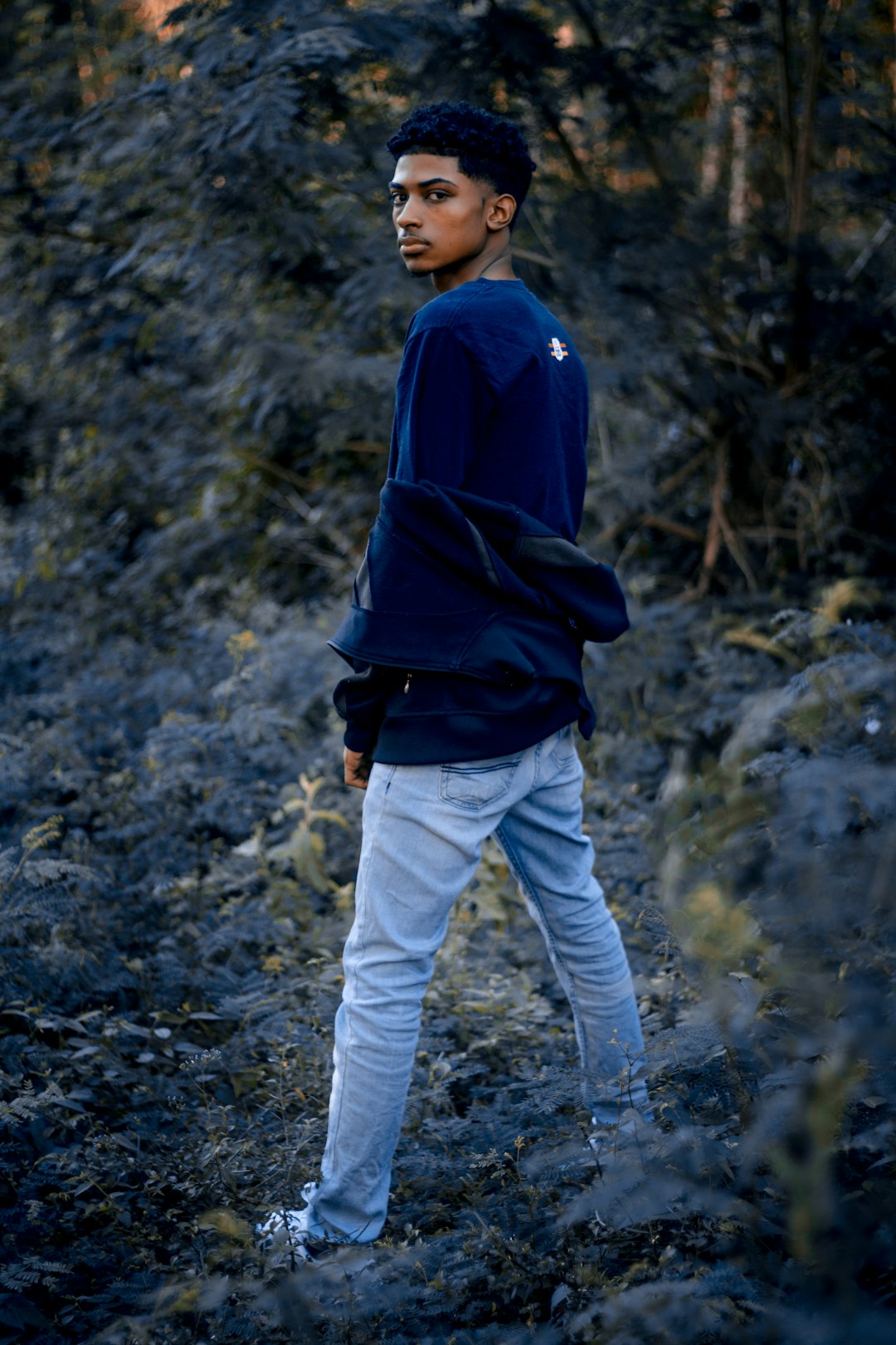man in blue hoodie and white pants standing on rocky ground