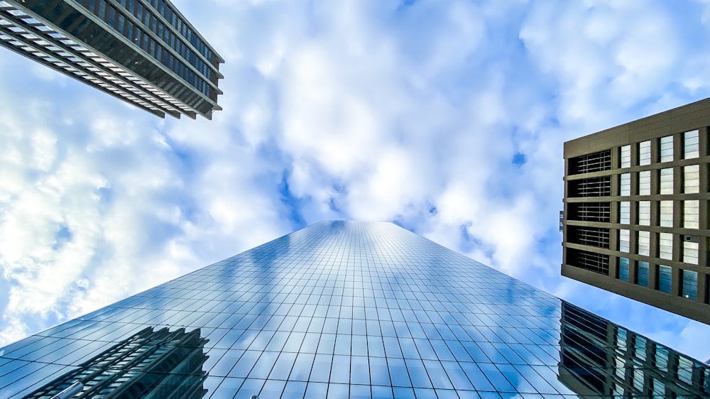 Photographie en contre-plongée d’un bâtiment en verre bleu sous des nuages blancs et un ciel bleu pendant la journée
