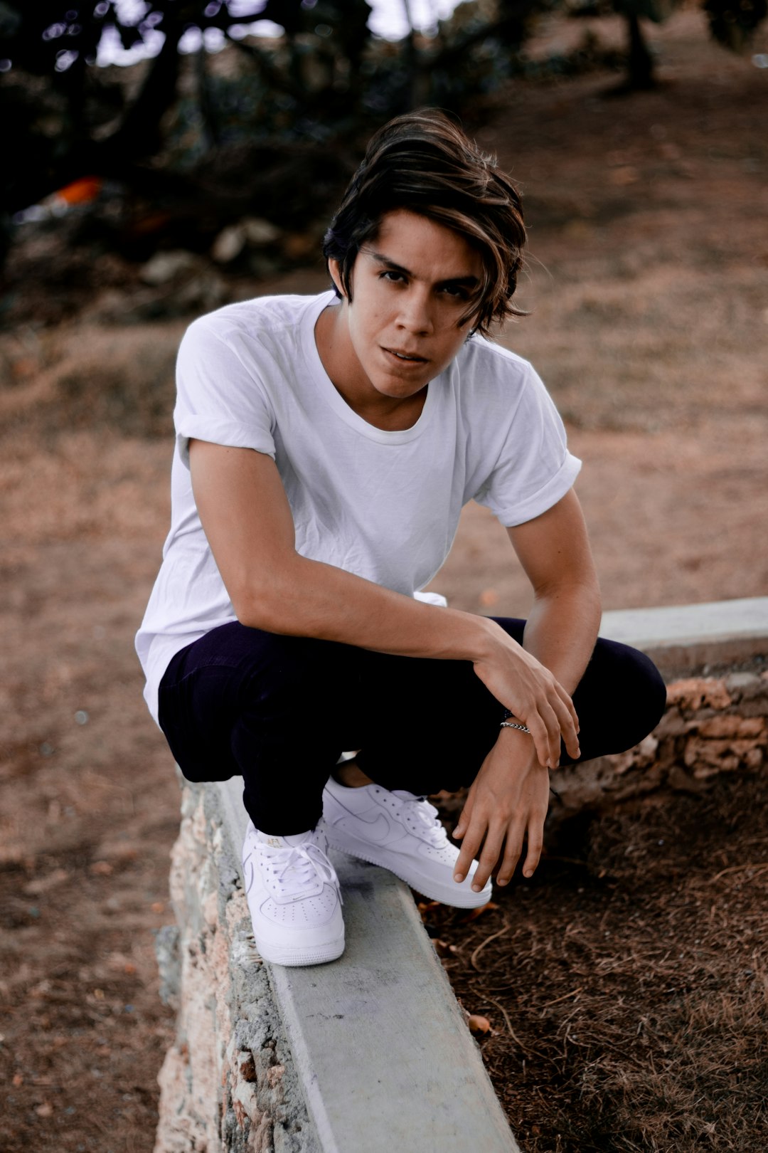 man in white crew neck t-shirt and black pants sitting on brown rock during daytime