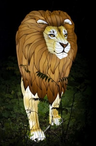 A luminous lion sculpture positioned amidst a backdrop of dark foliage. The lion features a detailed mane with varying shades and expressive eyes, creating a striking glow against the night scenery.
