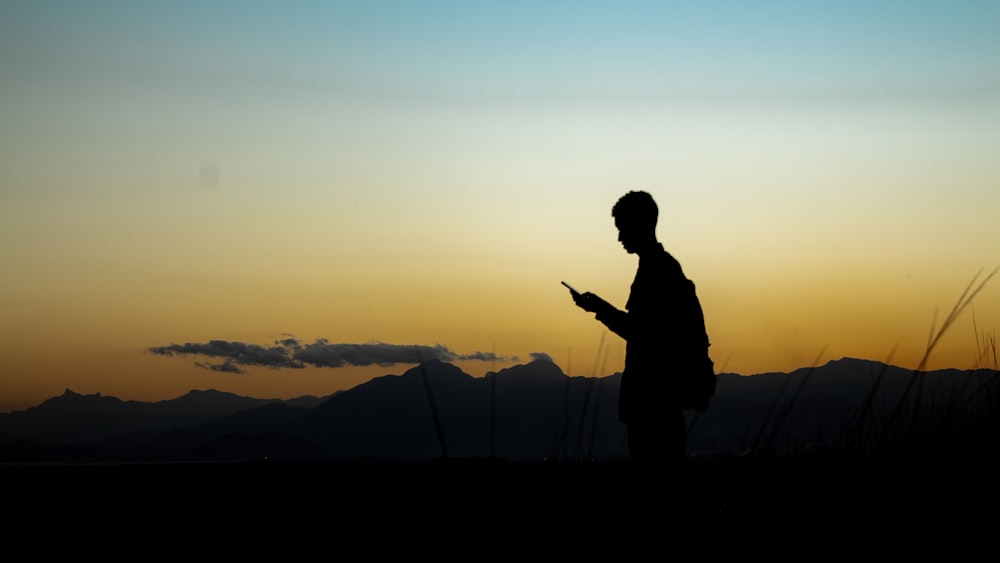 silhouette of man standing on hill during sunset