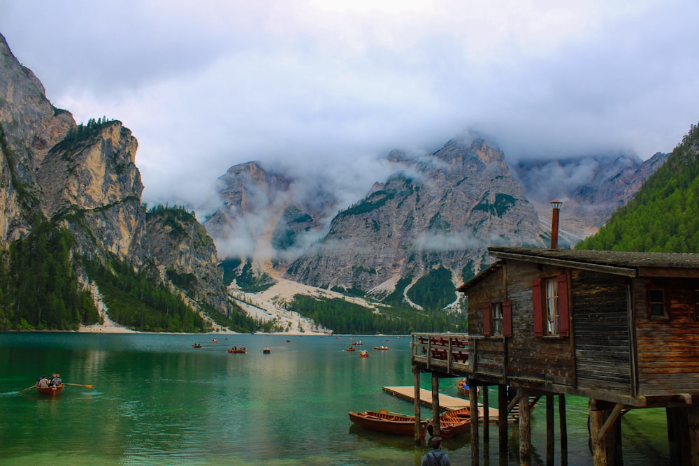 brown wooden house on dock near body of water and mountains during daytime